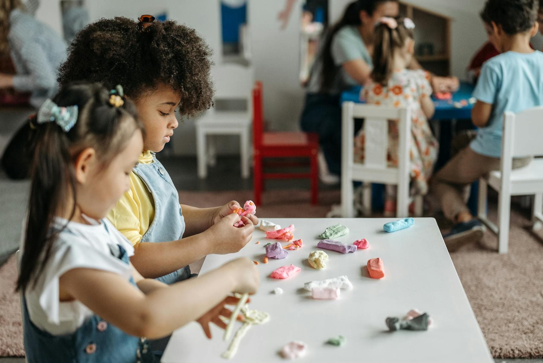 Two young children work side by side at a colorful preschool table.