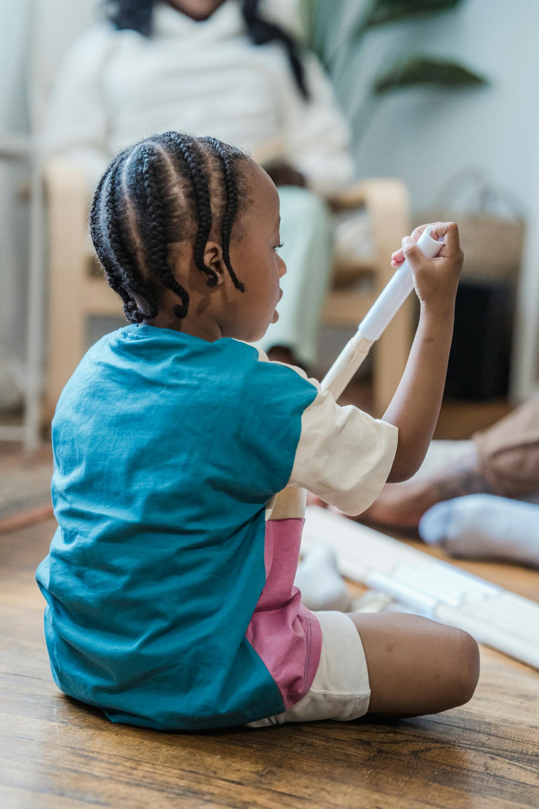 A young child sits on the floor concentrating on a drawing with markers.